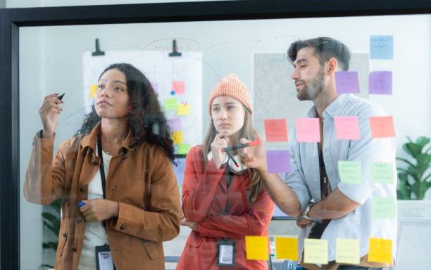featured-image-1763953213 Multiethnic young business people brainstorming on a project by writing on the glass wall in the office.