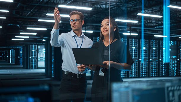 featured-image-1772575288 Information Technology Engineer and System Administrator Monitoring Web Services Cloud Solution Software and Sharing Ideas with Each Other in Big Data Center Server. People Use Laptop.