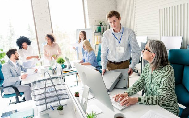 Group of professionals in a corporate office environment collaborating and focusing on various work tasks, demonstrating teamwork and productivity in a modern workplace setting.