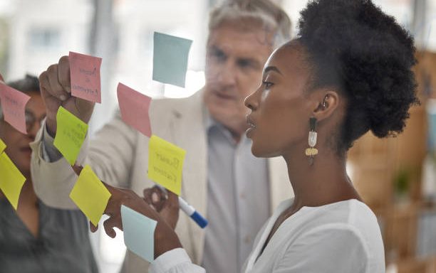 Meeting, planning and glass with a black woman leading a presentation in a boardroom for company strategy. Teamwork, presentation and sticky notes in an office with a female employee talking to staff